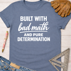 Women's funny woodworking graphic tee shirt for female woodworkers, makers, and DIY builders — Sawdust & Ponytails. Blue cotton t-shirt with "Built With Bad Math And Pure Determination" in white text.