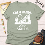 Sage green "Calm Hands Sharp Skills" t-shirt with a hand plane graphic, styled with jeans and tools.