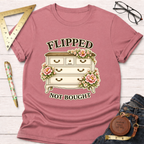 Pink "Flipped Not Bought" t-shirt with a vintage dresser and floral design, styled on a white wooden surface.