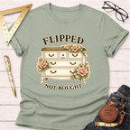 Sage green t-shirt with "Flipped Not Bought" text and a vintage dresser adorned with pink flowers.