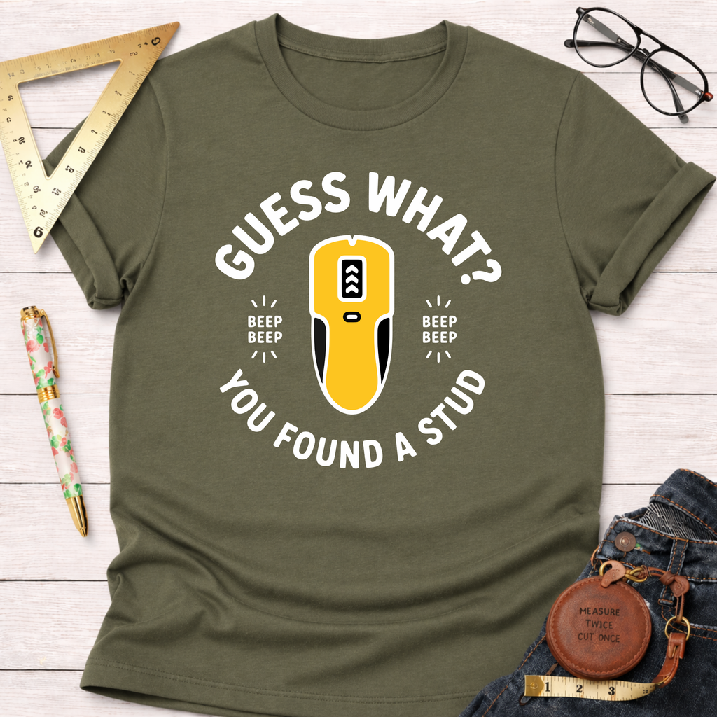 Olive green "Guess What? You Found A Stud" t-shirt with a yellow stud finder graphic, styled with jeans and tools.