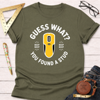 Olive green "Guess What? You Found A Stud" t-shirt with a yellow stud finder graphic, styled with jeans and tools.