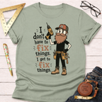 Sage green cotton t-shirt with a cartoon carpenter holding a drill and the text "I don't have to fix things. I get to fix things.