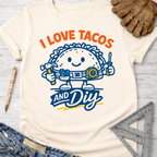 Women's funny woodworking graphic tee shirt for female woodworkers, makers, and DIY builders — Sawdust & Ponytails. Cream short-sleeve tee with "I Love Tacos And DIY" text and a happy taco character holding tools.