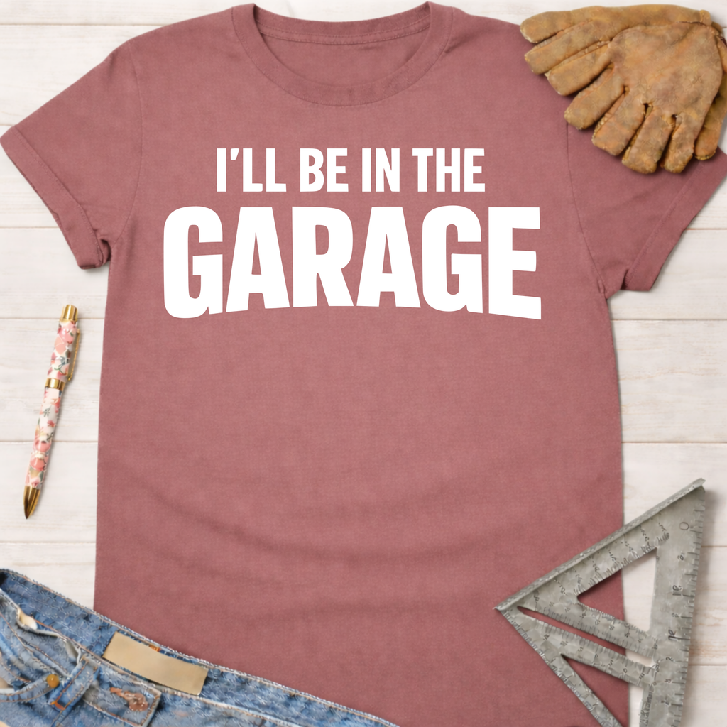 Women's funny woodworking graphic tee shirt for female woodworkers, makers, and DIY builders — Sawdust & Ponytails. Mauve short-sleeve t-shirt with "I'LL BE IN THE GARAGE" in white text.