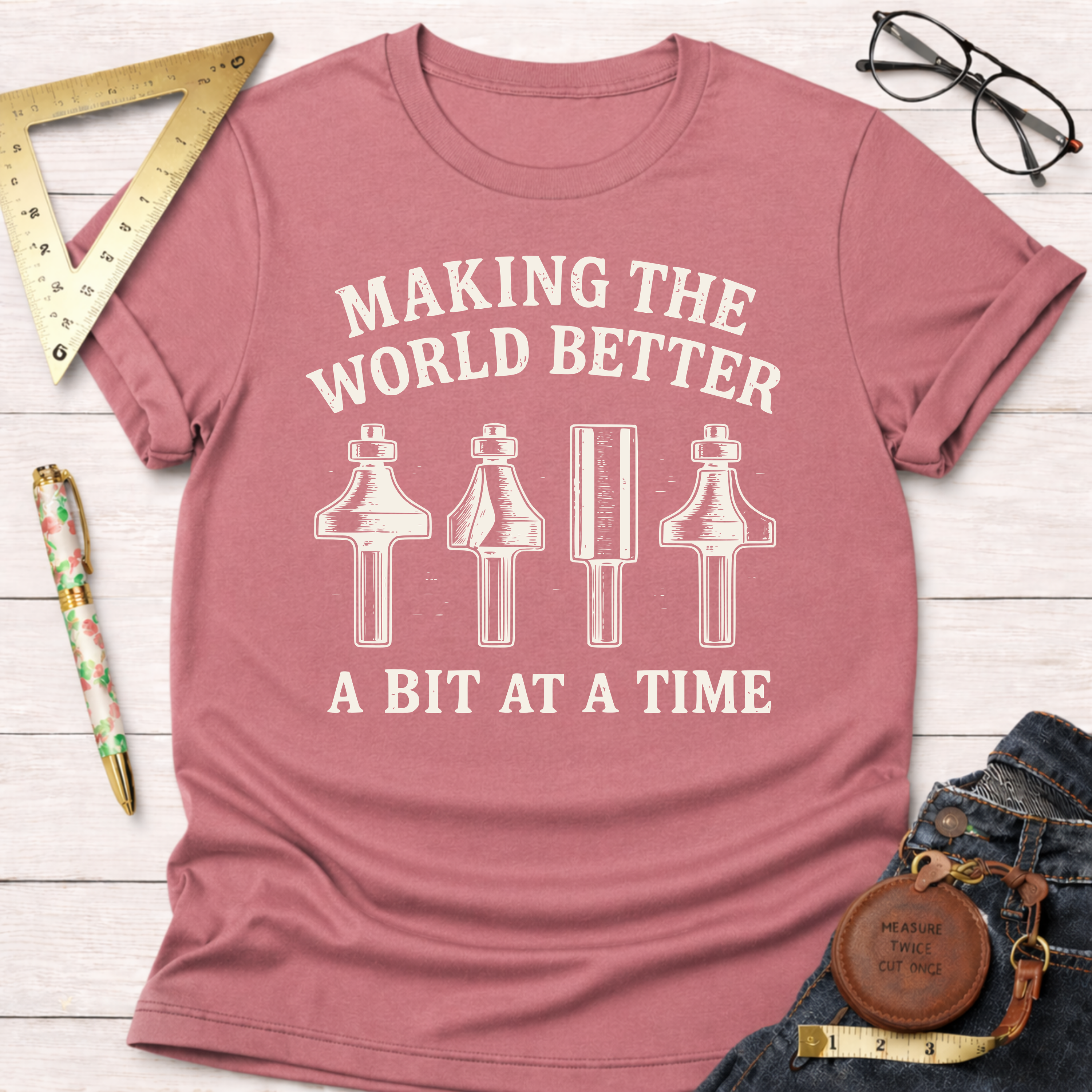 Women's funny woodworking graphic tee shirt for female woodworkers, makers, and DIY builders — Sawdust & Ponytails. Heather mauve t-shirt with "Making The World Better A Bit At A Time" text and four router bit graphics.