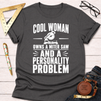 Dark gray cotton t-shirt with "Cool Woman Owns A Miter Saw And A Personality Problem" in white text.