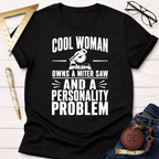Black cotton t-shirt with "Cool Woman Owns A Miter Saw And A Personality Problem" graphic.