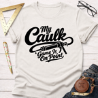 White cotton "My Caulk Game Is On Point" t-shirt with a black caulk gun graphic, styled with jeans and tools.