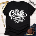 Black cotton "My Caulk Game Is On Point" t-shirt with a caulk gun graphic, displayed with carpentry tools.