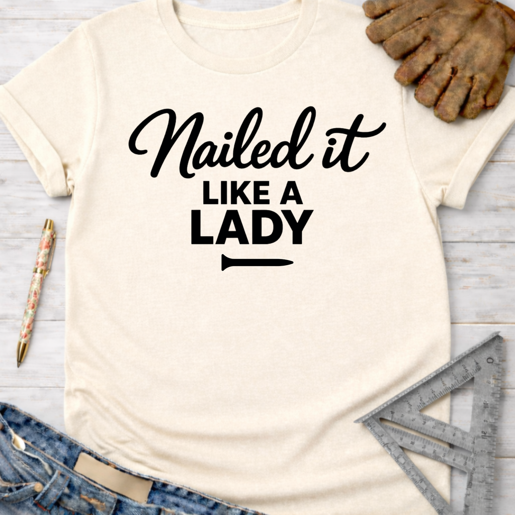 Women's funny woodworking graphic tee shirt for female woodworkers, makers, and DIY builders — Sawdust & Ponytails. Cream t-shirt with "Nailed it Like a Lady" in black script, styled with jeans, work gloves, and tools.