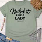 Women's funny woodworking graphic tee shirt for female woodworkers, makers, and DIY builders — Sawdust & Ponytails. Sage green cotton tee with "Nailed it LIKE A LADY" in black script.