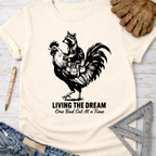 Women's funny woodworking graphic tee shirt for female woodworkers, makers, and DIY builders — Sawdust & Ponytails. Cream unisex tee with a raccoon riding a rooster, "Living The Dream One Bad Cut At A Time" text.