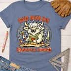 Women's funny woodworking graphic tee shirt for female woodworkers, makers, and DIY builders — Sawdust & Ponytails. Blue short-sleeve t-shirt with a cartoon highland cow building, text "She Builds Beautiful Things".