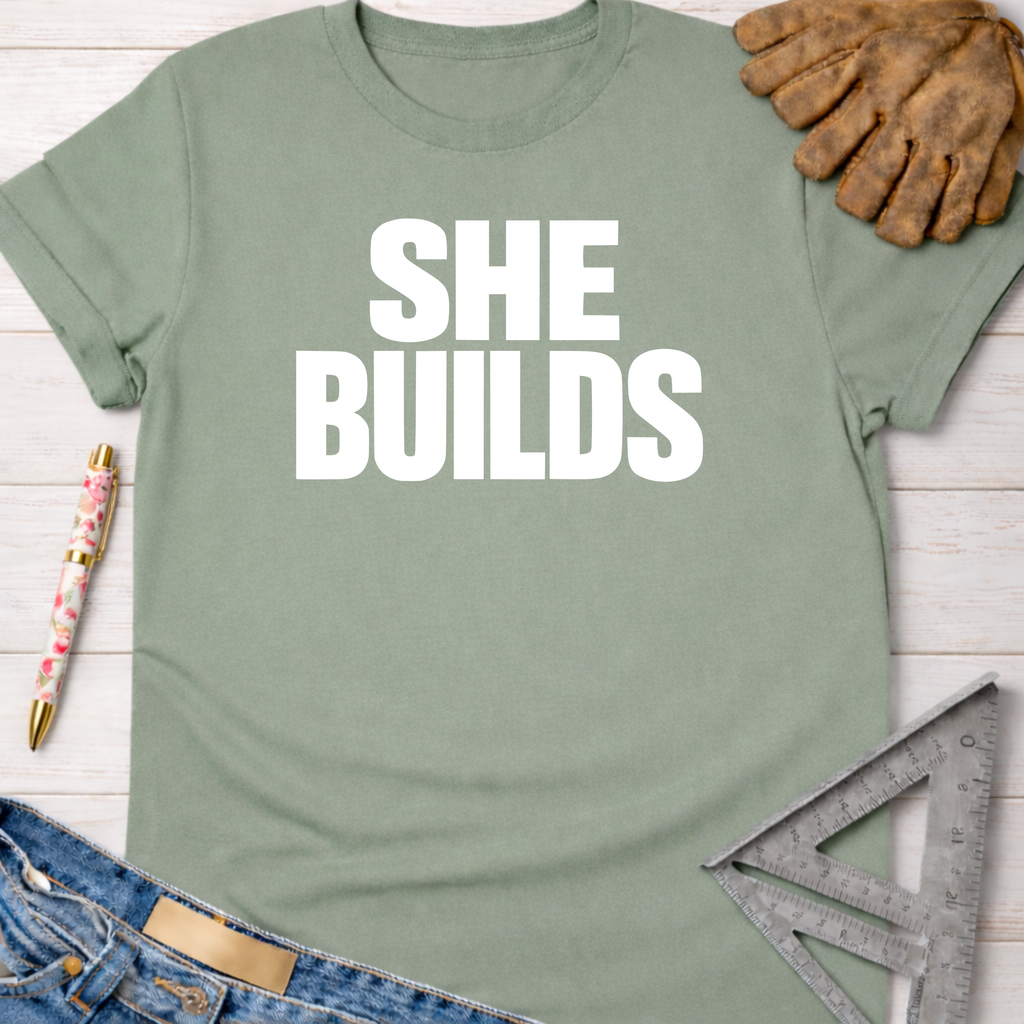 Sage green "SHE BUILDS" graphic tee with work gloves, jeans, pen, and ruler. Women's funny woodworking graphic tee shirt for female woodworkers, makers, and DIY builders — Sawdust & Ponytails
