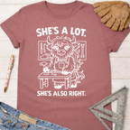 Women's funny woodworking graphic tee shirt for female woodworkers, makers, and DIY builders — Sawdust & Ponytails. Mauve cotton tee with "She's A Lot. She's Also Right." and a cartoon yak at a workbench.