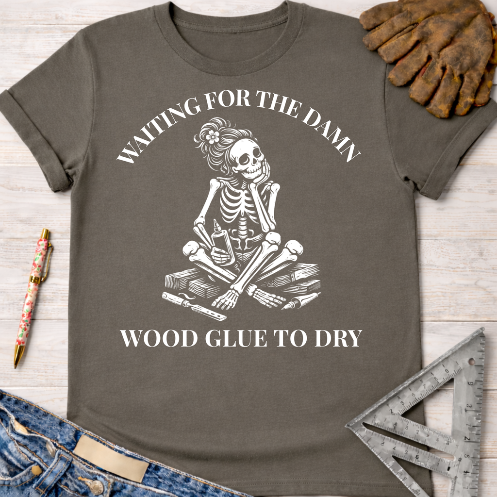 Women's funny woodworking graphic tee shirt for female woodworkers, makers, and DIY builders — Sawdust & Ponytails. Dark gray t-shirt with a white graphic of a bored skeleton waiting for wood glue to dry.