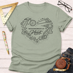 Sage green "Woodworker At Heart" t-shirt with heart-shaped tools design, flat lay on white wood.