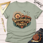 Sage green cotton t-shirt with "Woodworking Awaits" graphic featuring mountains, saw blade sun, and hand plane.
