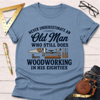 Light blue cotton t-shirt with "Never Underestimate An Old Man Who Still Does Woodworking In His Eighties" text and tools.
