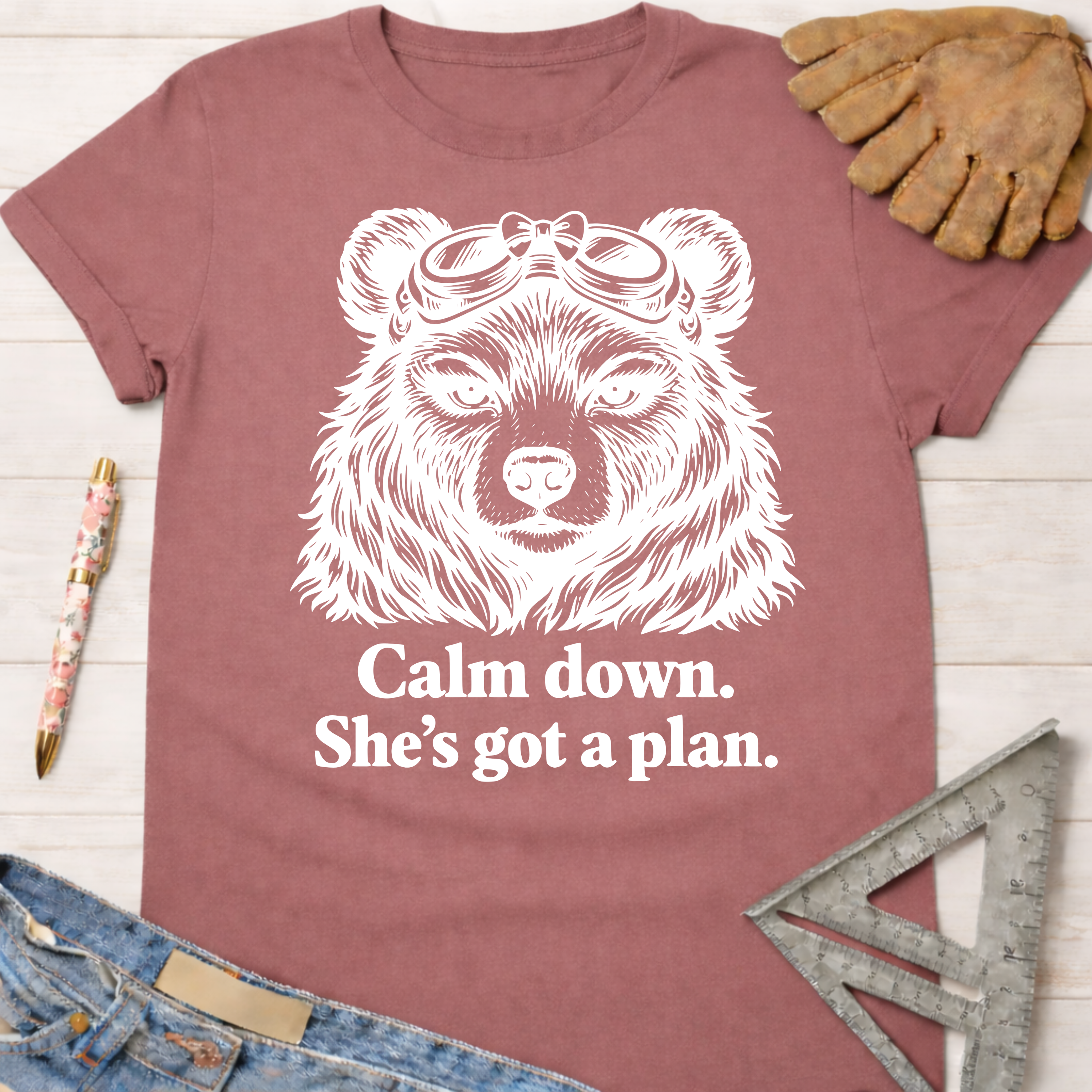 Women's funny woodworking graphic tee shirt for female woodworkers, makers, and DIY builders — Sawdust & Ponytails. Mauve t-shirt with a white graphic of a bear wearing goggles and the text "Calm down. She's got a plan.