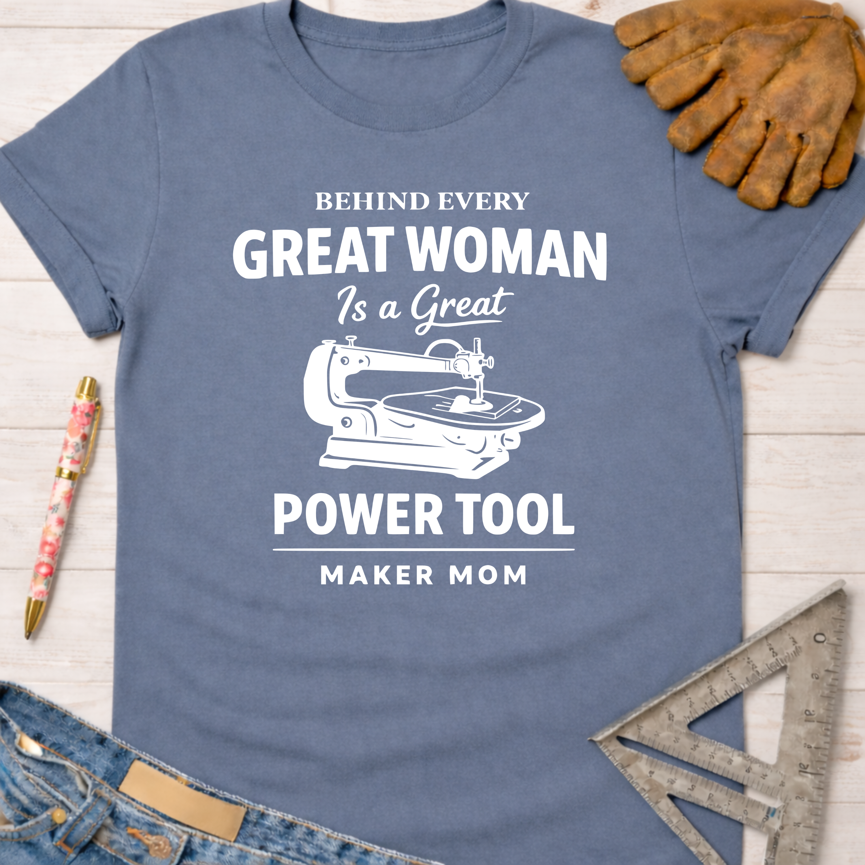 Women's funny woodworking graphic tee shirt for female woodworkers, makers, and DIY builders — Sawdust & Ponytails. Blue cotton tee with "Behind Every Great Woman Is a Great Power Tool Maker Mom" text and sewing machine graphic.