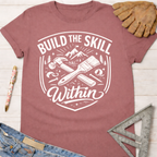 Women's funny woodworking graphic tee shirt for female woodworkers, makers, and DIY builders — Sawdust & Ponytails. Mauve t-shirt with "Build the Skill Within" graphic, hammer, paintbrush, and mountains.