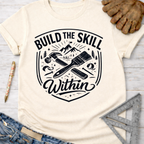 Women's funny woodworking graphic tee shirt for female woodworkers, makers, and DIY builders — Sawdust & Ponytails. Cream t-shirt with "Build the Skill Within" graphic featuring hammer, paintbrush, and mountains.