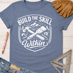 Women's funny woodworking graphic tee shirt for female woodworkers, makers, and DIY builders — Sawdust & Ponytails. Blue cotton tee with "Build the Skill Within" graphic featuring a hammer, paintbrush, and mountains.