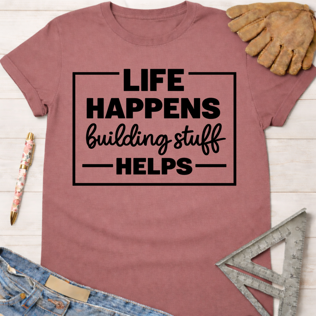 Women's funny woodworking graphic tee shirt for female woodworkers, makers, and DIY builders — Sawdust & Ponytails. Mauve short-sleeve tee with "Life Happens Building Stuff Helps" text.
