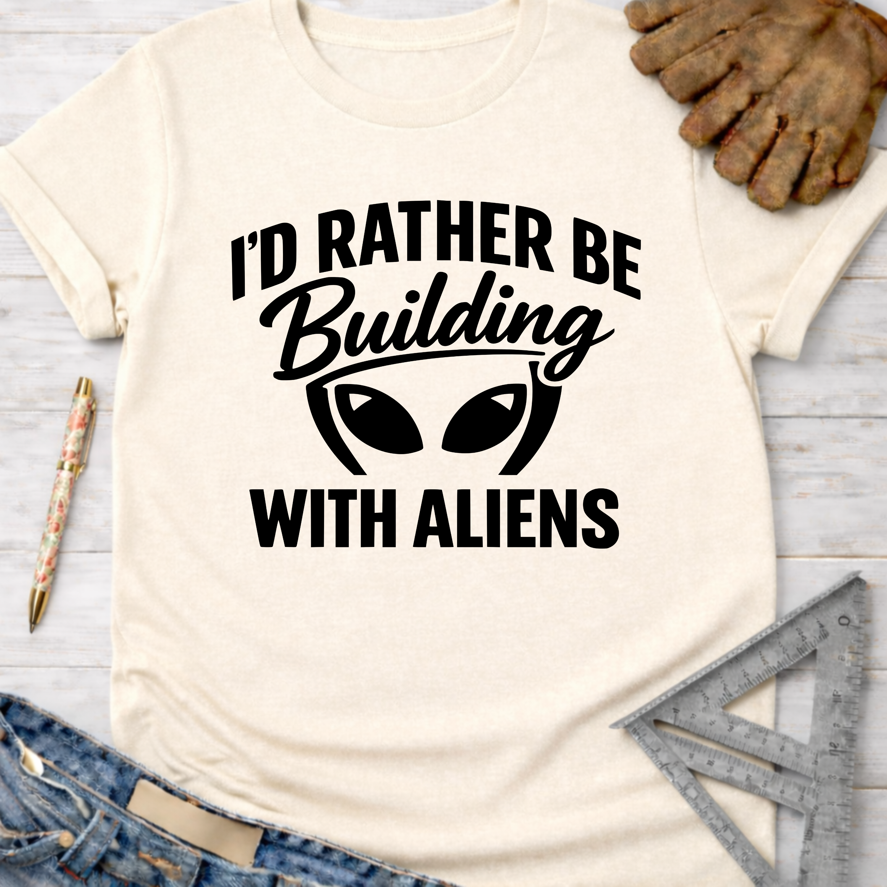 Women's funny woodworking graphic tee shirt for female woodworkers, makers, and DIY builders — Sawdust & Ponytails. Cream t-shirt with "I'd Rather Be Building With Aliens" graphic.