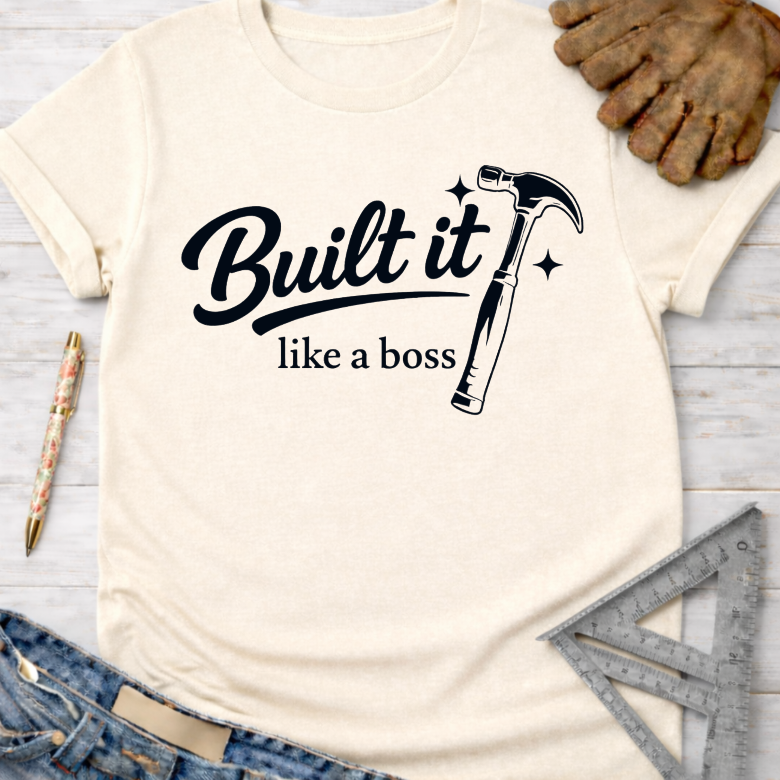 Women's funny woodworking graphic tee shirt for female woodworkers, makers, and DIY builders — Sawdust & Ponytails. Cream t-shirt with "Built it like a boss" text and hammer graphic.