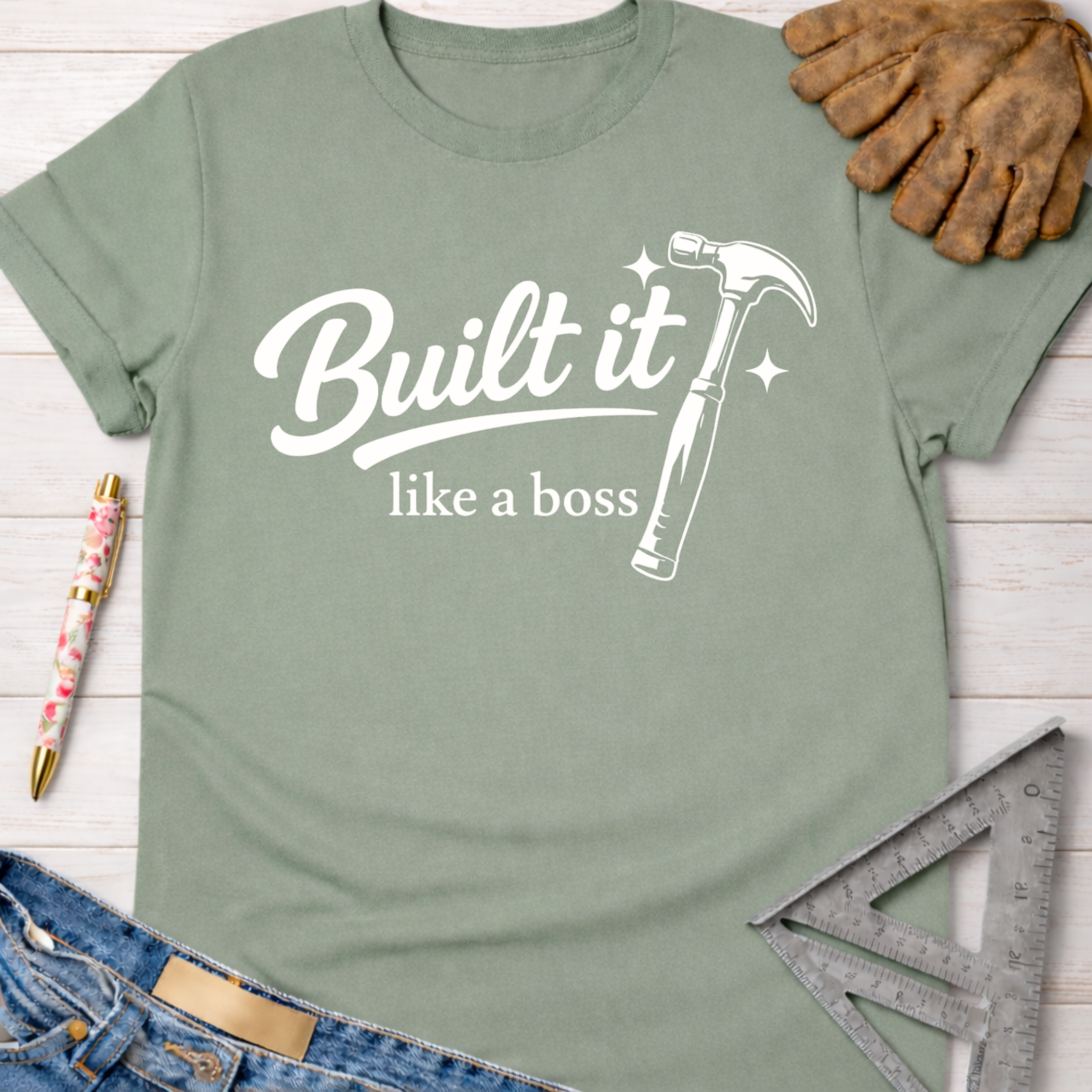 Women's funny woodworking graphic tee shirt for female woodworkers, makers, and DIY builders — Sawdust & Ponytails. Sage green cotton t-shirt with "Built it like a boss" text and hammer graphic.