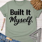 Women's funny woodworking graphic tee shirt for female woodworkers, makers, and DIY builders — Sawdust & Ponytails. Sage green "Built It Myself" graphic tee with work gloves, jeans, and a ruler.