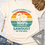 Women's funny woodworking graphic tee shirt for female woodworkers, makers, and DIY builders — Sawdust & Ponytails. Cream short-sleeve tee with a retro sunset graphic and "Today's Forecast: 100% Chance of Sawdust in the Bra" text.