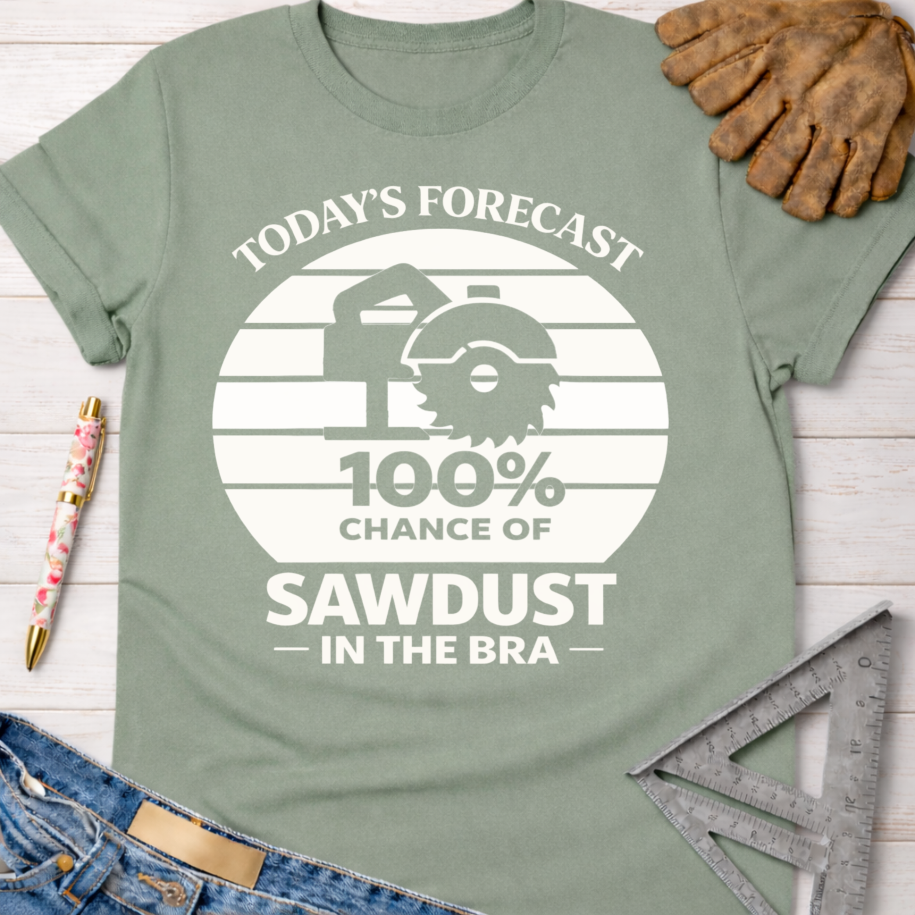 Women's funny woodworking graphic tee shirt for female woodworkers, makers, and DIY builders — Sawdust & Ponytails. Sage green t-shirt with "Today's Forecast 100% Chance of Sawdust in the Bra" graphic.