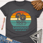 Women's funny woodworking graphic tee shirt for female woodworkers, makers, and DIY builders — Sawdust & Ponytails. Dark gray t-shirt with a retro sunset graphic featuring a saw and "Today's Forecast: 100% Chance of Sawdust in the Bra.