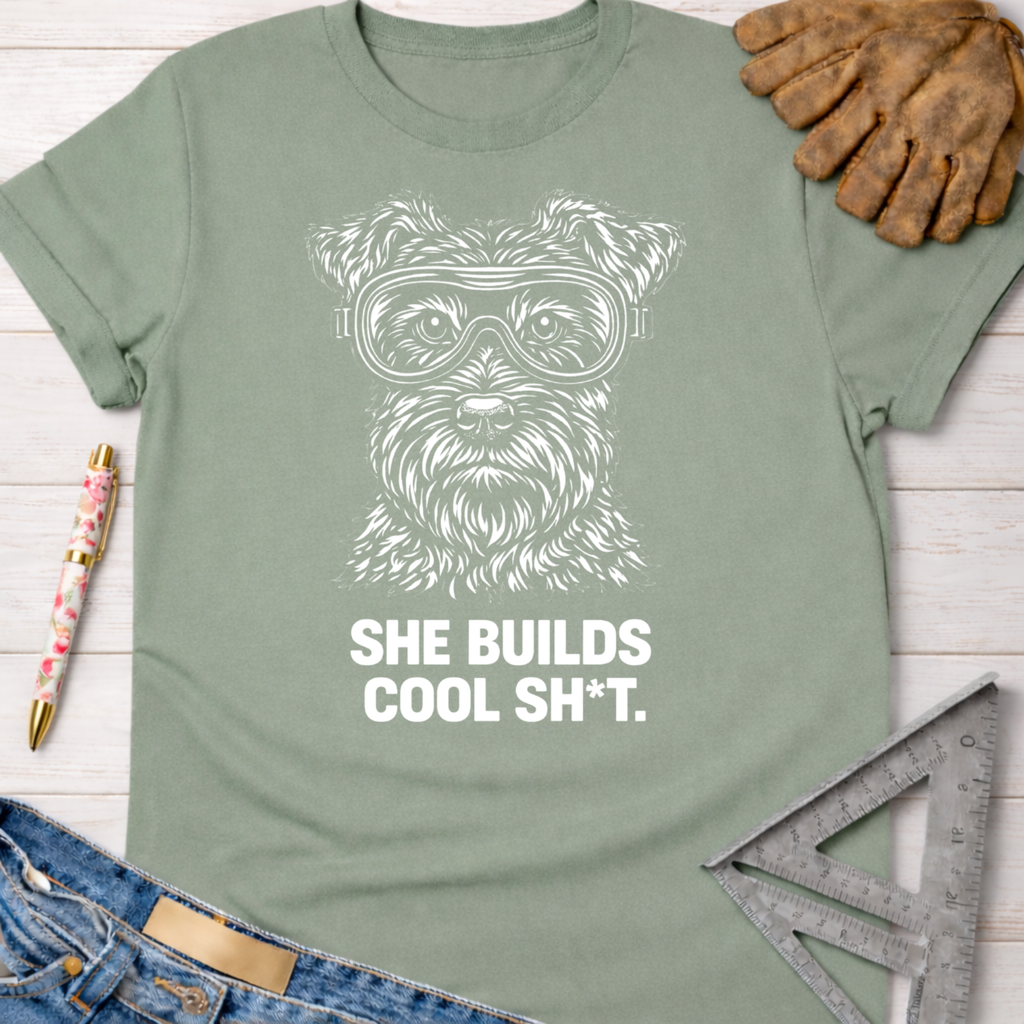 Sage green cotton tee with white graphic of a dog in goggles and "SHE BUILDS COOL SH*T." Women's funny woodworking graphic tee shirt for female woodworkers, makers, and DIY builders — Sawdust & Ponytails
