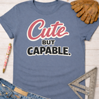 Women's funny woodworking graphic tee shirt for female woodworkers, makers, and DIY builders — Sawdust & Ponytails. Blue cotton t-shirt with "Cute BUT CAPABLE." in pink and black text.