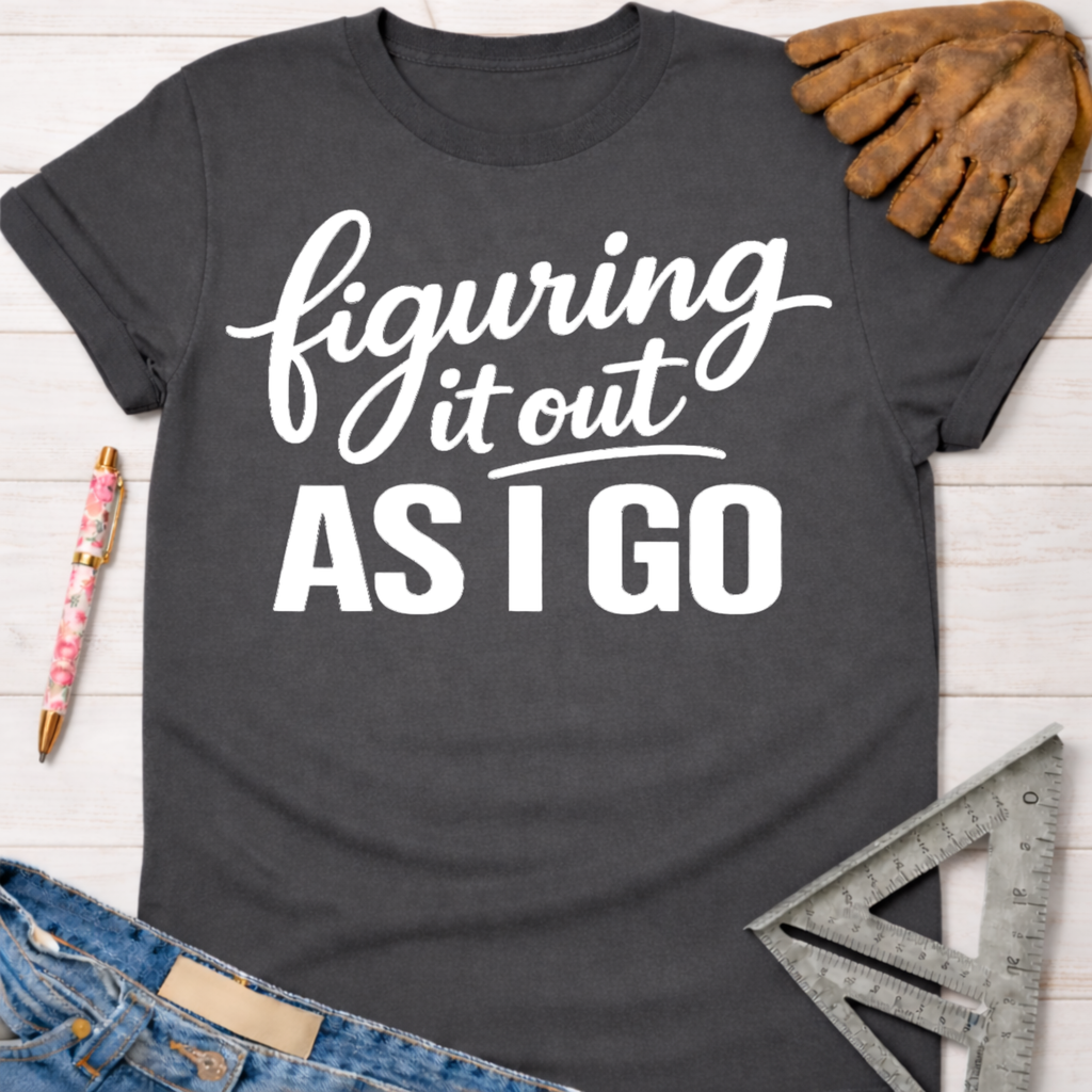 Women's funny woodworking graphic tee shirt for female woodworkers, makers, and DIY builders — Sawdust & Ponytails. Dark gray t-shirt with "figuring it out AS I GO" in white script.