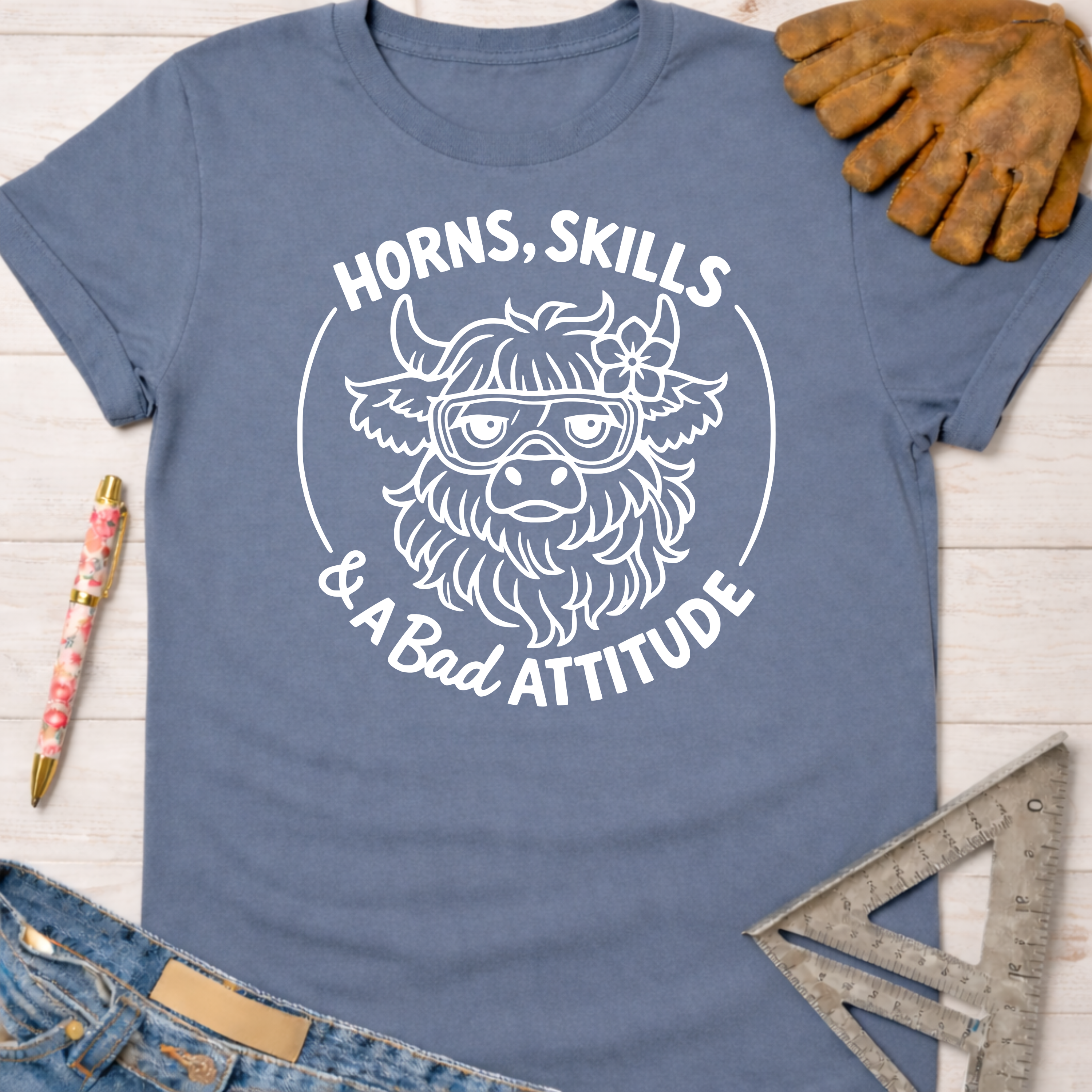 Women's funny woodworking graphic tee shirt for female woodworkers, makers, and DIY builders — Sawdust & Ponytails. Blue cotton tee with a white graphic of a horned animal wearing goggles and a flower, text reads "Horns, Skills & A Bad Attitude.