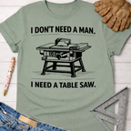 Women's funny woodworking graphic tee shirt for female woodworkers, makers, and DIY builders — Sawdust & Ponytails. Sage green cotton t-shirt with "I DON'T NEED A MAN. I NEED A TABLE SAW." text and table saw graphic.