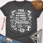 Women's funny woodworking graphic tee shirt for female woodworkers, makers, and DIY builders — Sawdust & Ponytails. Dark gray cotton tee with "YES I REALLY DO NEED ALL THESE Power Tools" and tool graphics.