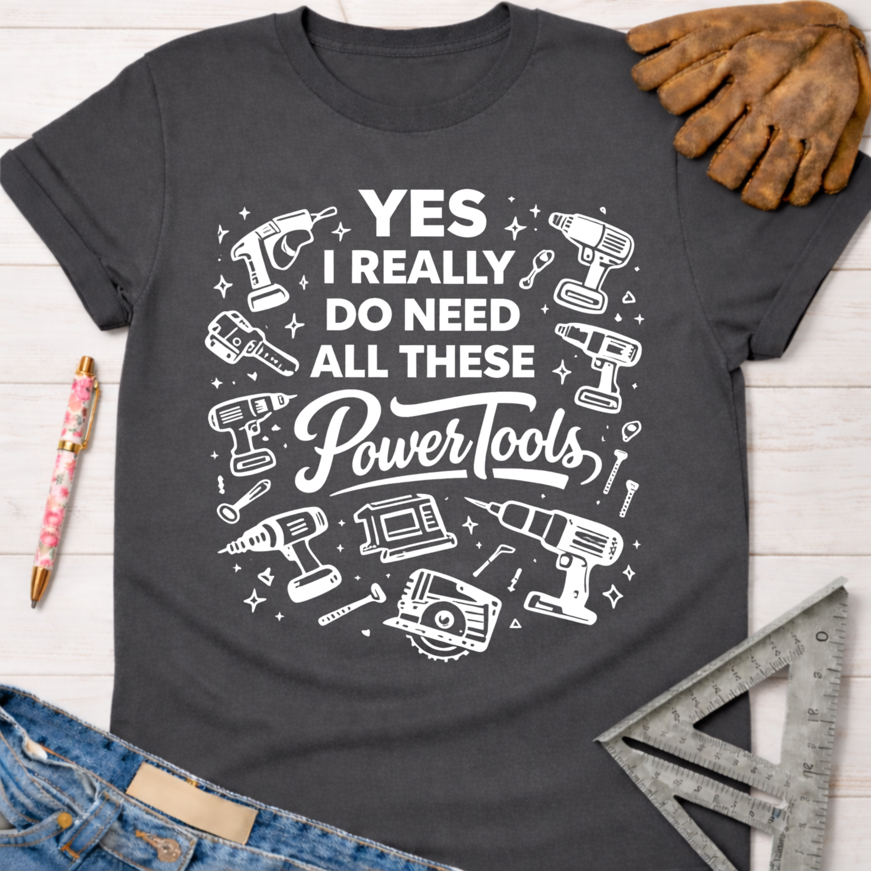 Women's funny woodworking graphic tee shirt for female woodworkers, makers, and DIY builders — Sawdust & Ponytails. Dark gray cotton tee with "YES I REALLY DO NEED ALL THESE Power Tools" and tool graphics.