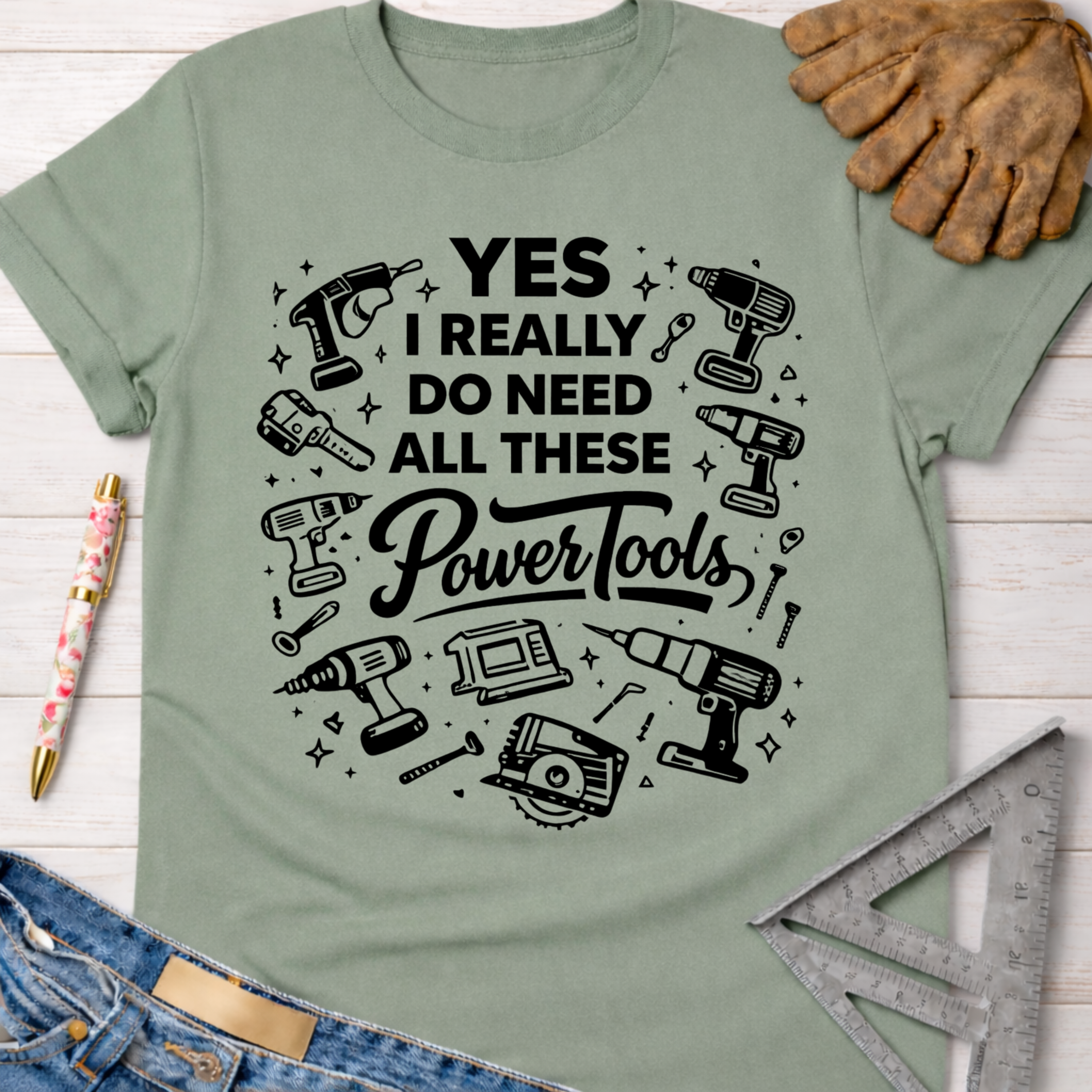 Women's funny woodworking graphic tee shirt for female woodworkers, makers, and DIY builders — Sawdust & Ponytails. Sage green cotton tee with "YES I REALLY DO NEED ALL THESE Power Tools" and tool graphics.