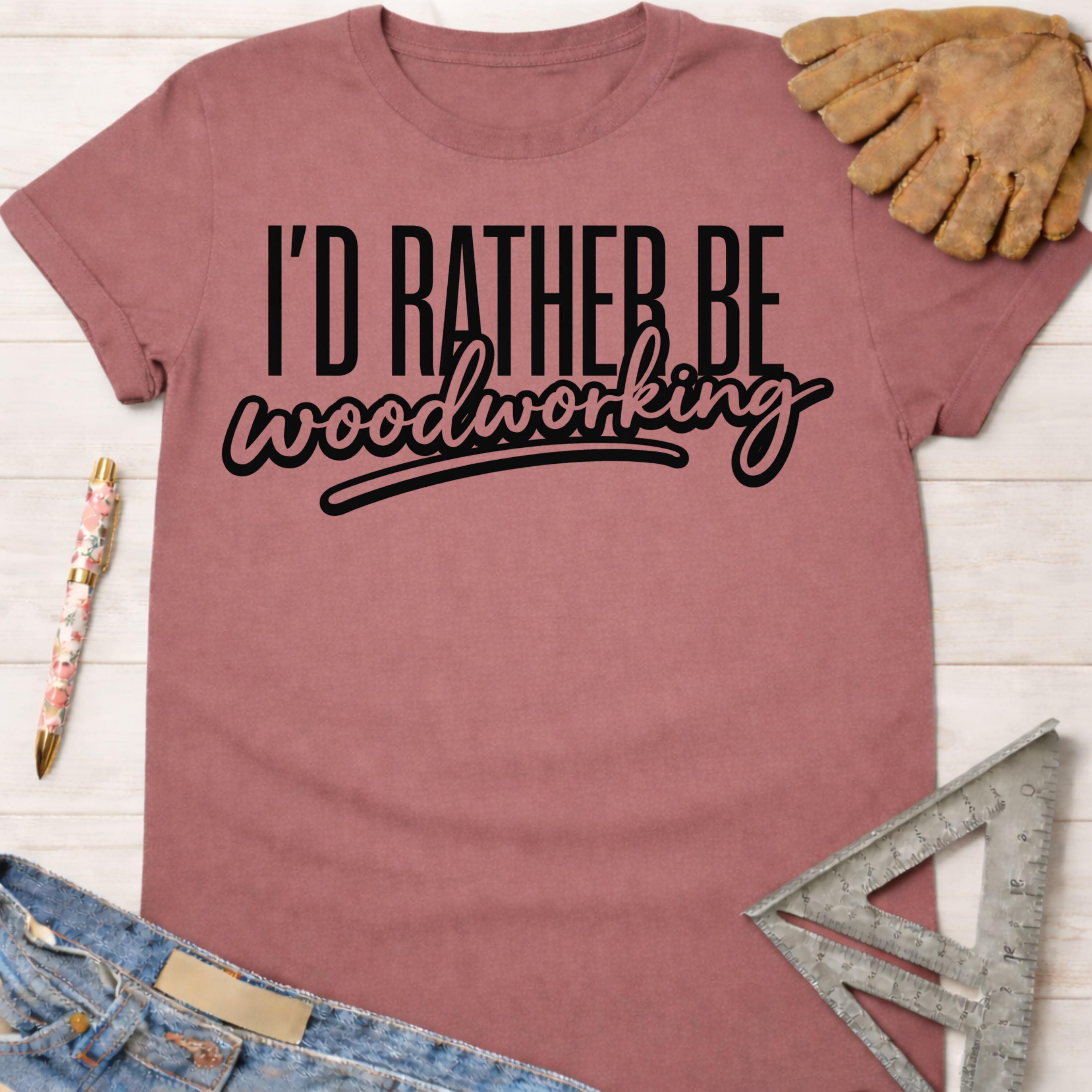 Women's funny woodworking graphic tee shirt for female woodworkers, makers, and DIY builders — Sawdust & Ponytails. Mauve pink cotton tee with "I'd Rather Be Woodworking" in black text.