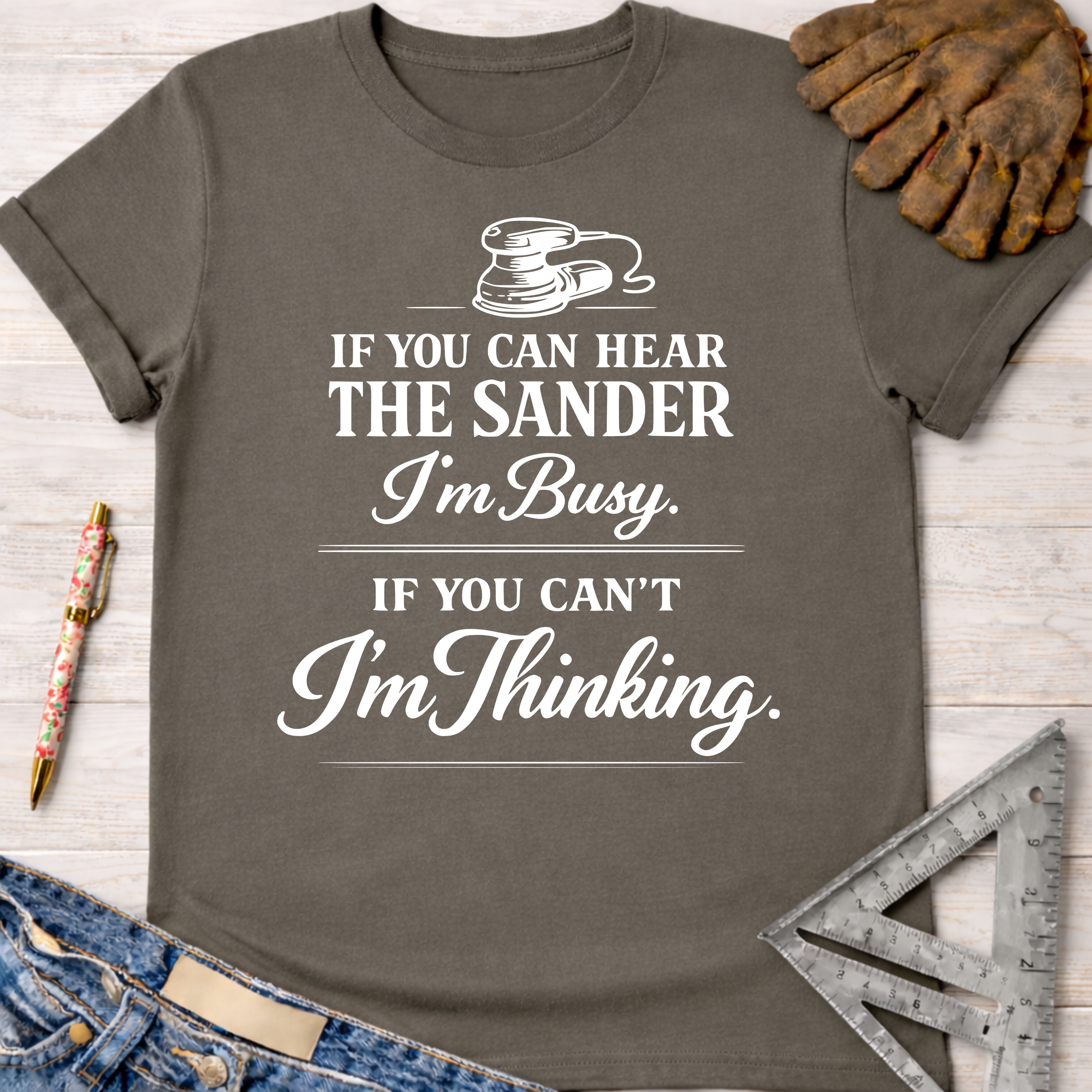 Women's funny woodworking graphic tee shirt for female woodworkers, makers, and DIY builders — Sawdust & Ponytails. Dark gray cotton tee with "If You Can Hear The Sander I'm Busy. If You Can't I'm Thinking." design.