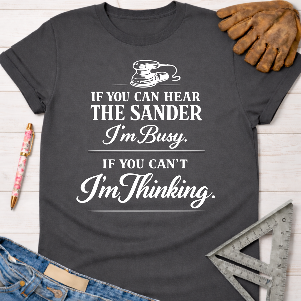 Women's funny woodworking graphic tee shirt for female woodworkers, makers, and DIY builders — Sawdust & Ponytails. Dark gray cotton tee with "If You Can Hear The Sander I'm Busy. If You Can't I'm Thinking." in white text.