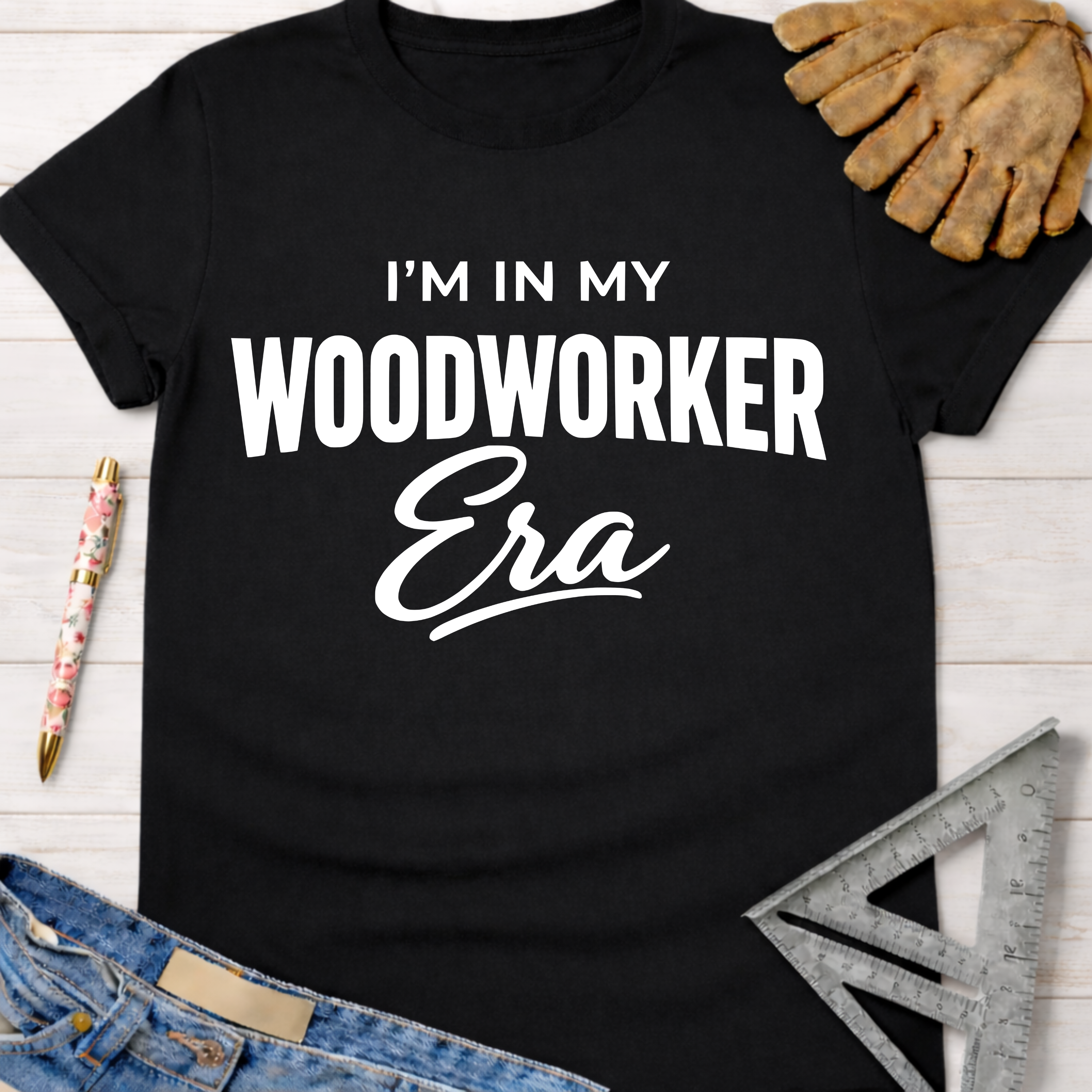 Black cotton "I'm In My Woodworker Era" graphic tee for women, with work gloves, ruler, and jeans.