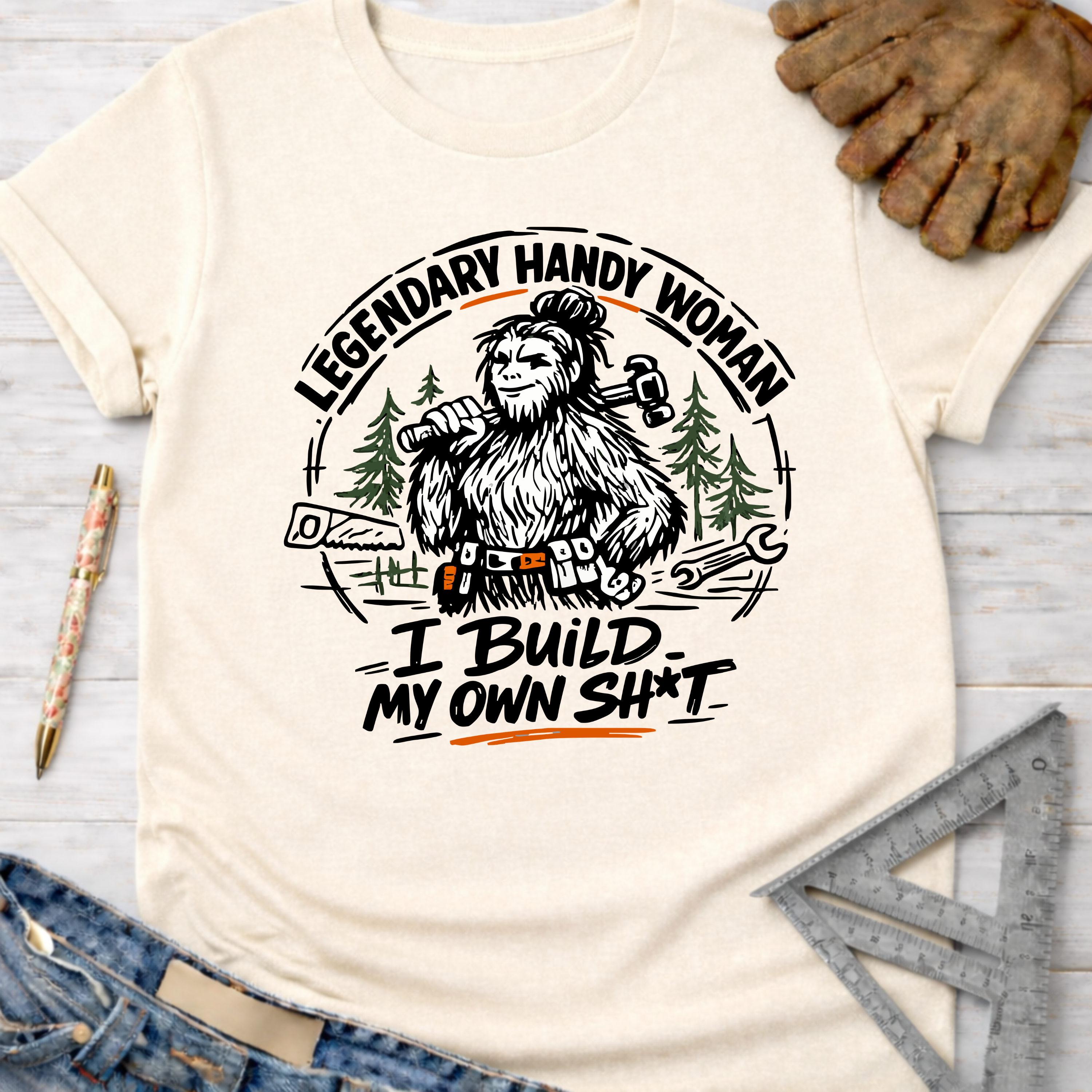 Cream t-shirt with "Legendary Handy Woman I Build My Own Sh*t" Bigfoot graphic. Women's funny woodworking graphic tee shirt for female woodworkers, makers, and DIY builders — Sawdust & Ponytails
